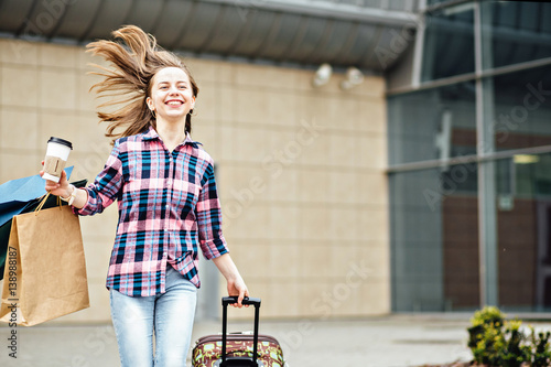 Happy hipster woman in plaid shirt running with disposable cups, suitcase and paperbag. Freedom Travel and Holiday Concept. © Iryna