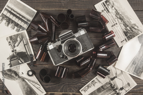 Old camera, film and black and white photographs are on the dark wooden surface