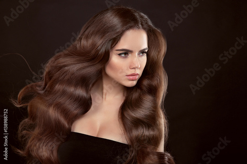 Healthy hair. Wavy hairstyle. Beautiful brunette woman with clean skin and shiny brown straight long hair isolated on black background.