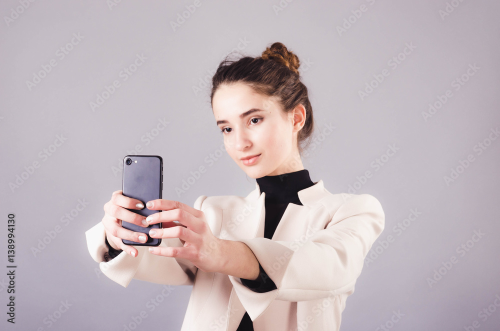 Portrait of a young attractive girl making selfie photo with smartphone isolated on a neutral gray background. Portrait of a young attractive girl making selfie photo with smartphone isolated on a neutral gray background.