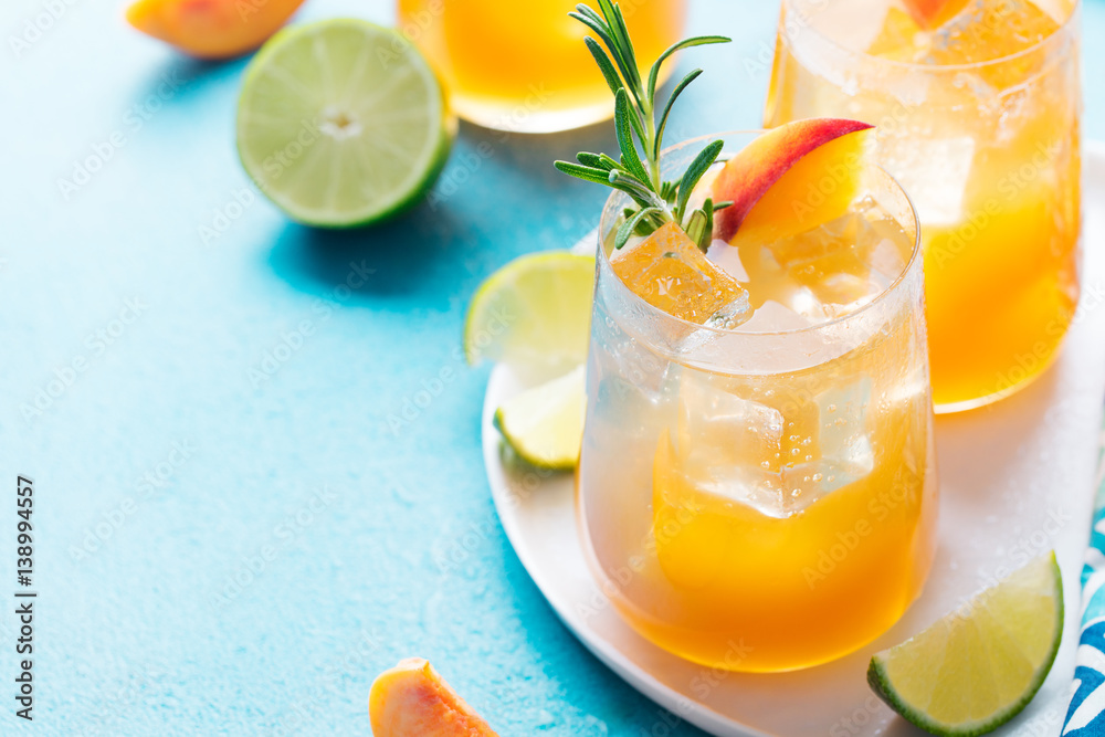 Fototapeta premium Peach cocktail, fizz, ice tea with fresh rosemary and lime. Blue background. Copy space.