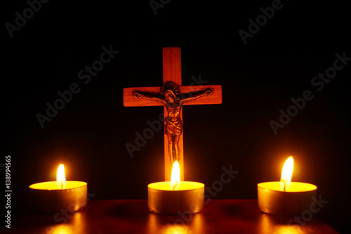 Crucifix and three burning candles in the darkness. Pray to Jesus Christ.