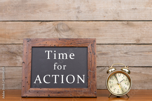 Alarm clock and blackboard with text "time for action" on brown wooden background