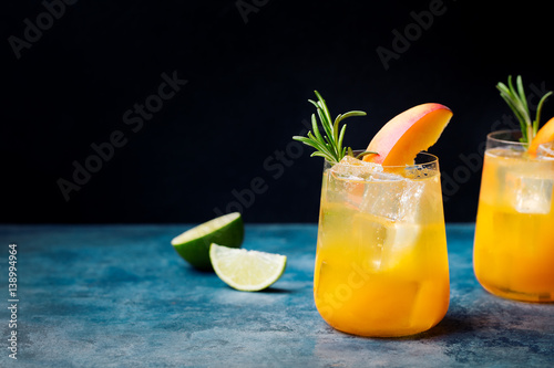 Peach cocktail, fizz with rosemary on blue stone background. Copy space