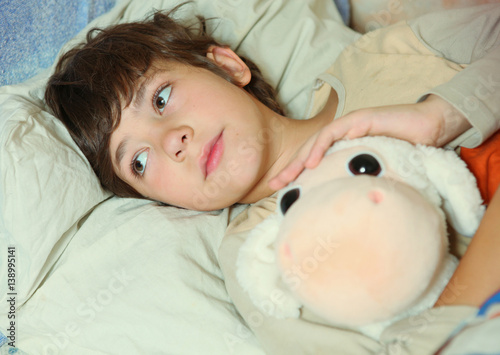preteen handsome boy sick in bed with sheep toy