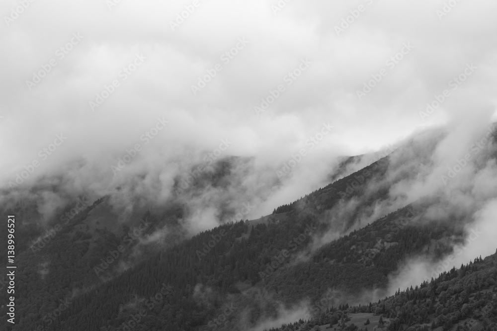Natural scenery with misty weather. Mist, fog and haze over peaks and summits of mountains. Mysterious atmosphere of black and white landscape
