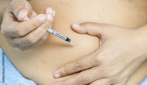 A lady is injecting insulin into her stomach. Photo is focus at syringe.
