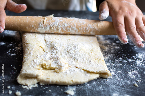 Person rolling pastry with rolling pin, close-up