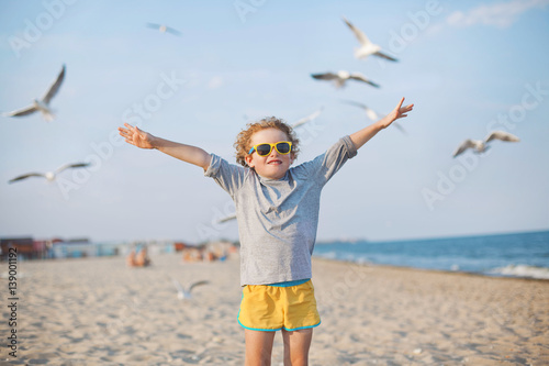 curly boy holds arms out like a bird, flying birds blurred in the background