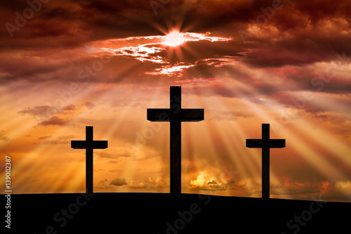 Jesus Christ cross on a background with dramatic sky,lighting,red, orange sunset,clouds,sunbeams,sun rays glowing behind three crosses on Golgotha mountain.Easter, resurrection, Good Friday concept.
