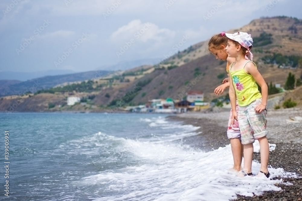 Children playing on the beach on the background of the village, throwing pebbles in the water.