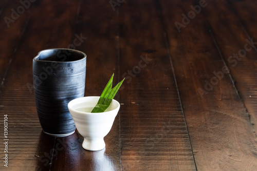 A black Sake jar and a white sake cup on the wood table.