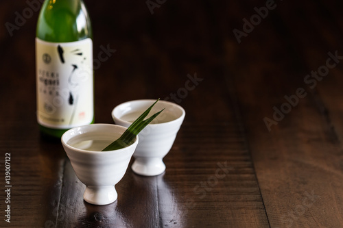 Two white sake cups and a bottle of sake on the rustic wood table.