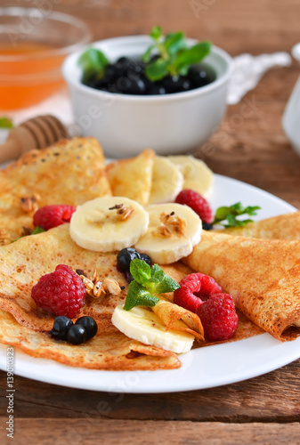 Homemade pancakes with banana, berries and honey for breakfast on a wooden background