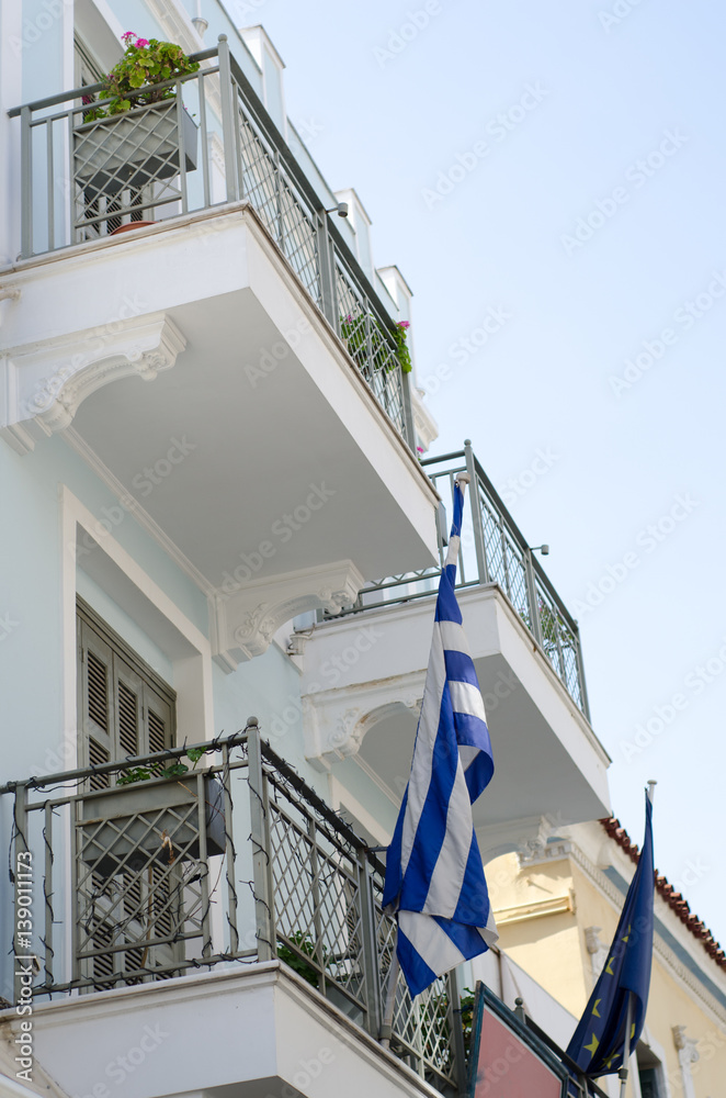 classical building in athens Greece, balcony with wooden window shutters, carved marbles down and greek flag