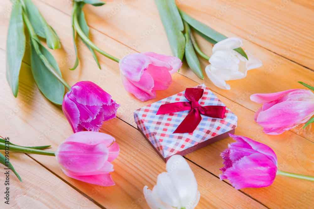 Bouquet of tender pink tulips with gift box on light wooden background