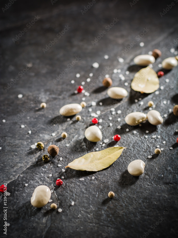 White beans and spices are scattered randomly on a black stone table from slate. White beans and spices are scattered randomly on a black stone table from slate.