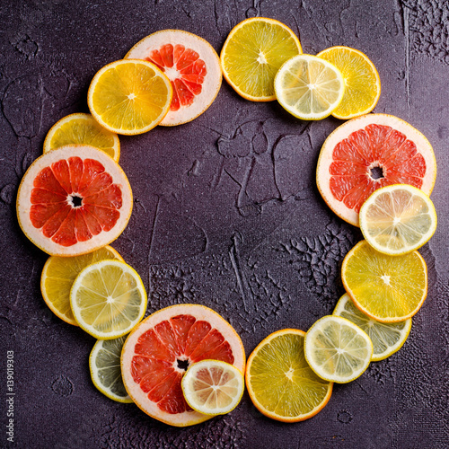 Citrus fruit slices of lemon, orange, grapefruit in circle shape on dark background.
