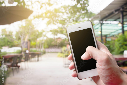 Mobile hold in hand with Coffee shop blur background