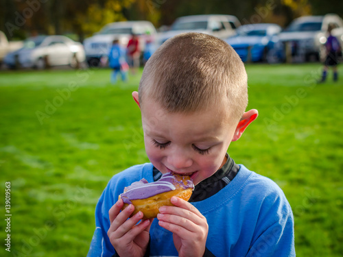 Young boy with ultra long eyelashes enjoying a donut in outdoor setting. Preschool youth completed soccer game, enjoying his reward.