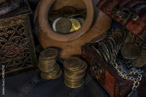 Treasure chest, pile and pillar of coins, a ceramic bowl filled with jewelry coins and candle lamp in dark environment 