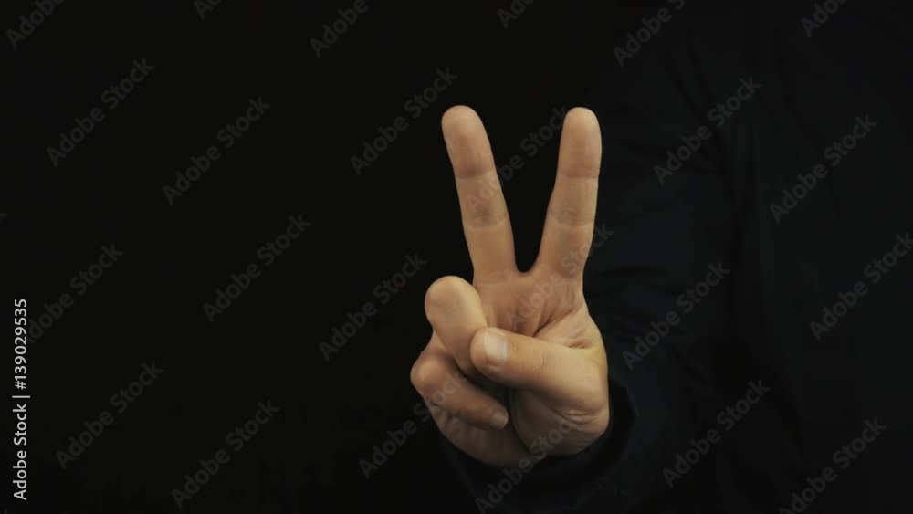 Caucasian male hand in long sleeve jacket make variety of positive finger gestures on black background, close up isolated. Okay, peace and horn signs, thumb up Caucasian male hand in long sleeve jacket make variety of positive finger gestures on black background, close up isolated. Okay, peace and horn signs, thumb up