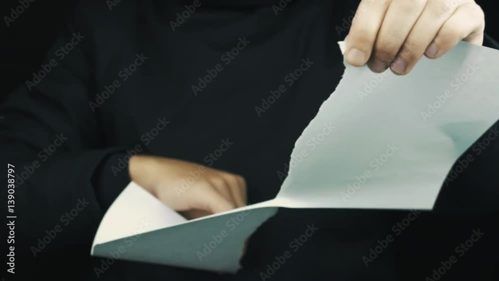 Caucasian man hands in long sleeve jacket ripping paper sheet, throws pieces on black background, close up isolated