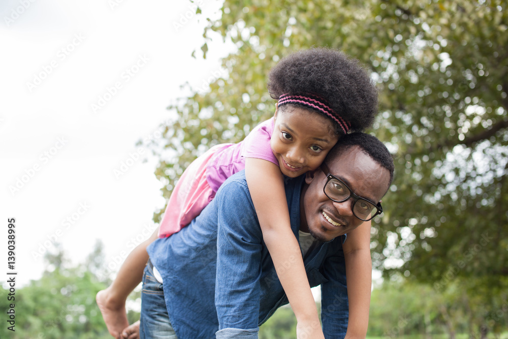 African American father and daughter playing and carrying on back in green park scene African American father and daughter playing and carrying on back in green park scene
