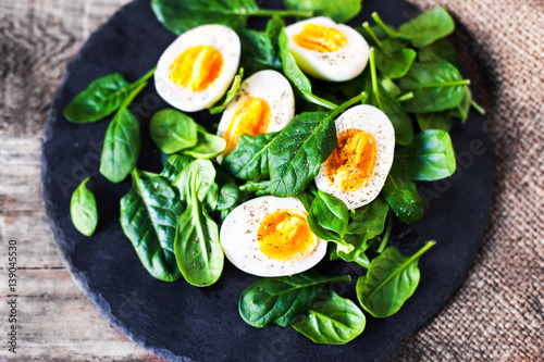  Boiled eggs cut in a half with Fresh green spinach baby leaves on wooden background with copy space