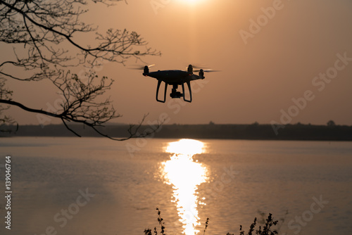 Modern drone watching the beautiful sunset. Silhouette Quad copter is flying above the lake at sunset.
