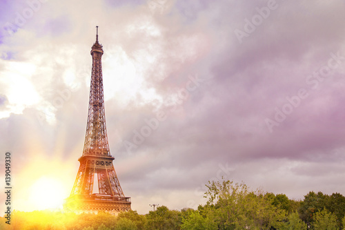 View on Eiffel tower over green summer trees with sunset rays. Beautiful Romantic background. Eiffel Tower from Champ de Mars, Paris, France.