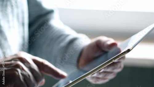 Elderly Man Text Messaging On Tablet. Bright Sunny Day, The Light Illuminates The Room.