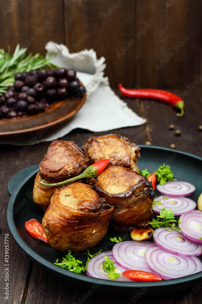 Juicy pork medallions wrapped in bacon, serve on the iron pan on the dark wooden dackground. Juicy pork medallions wrapped in bacon, serve on the iron pan on the dark wooden dackground.