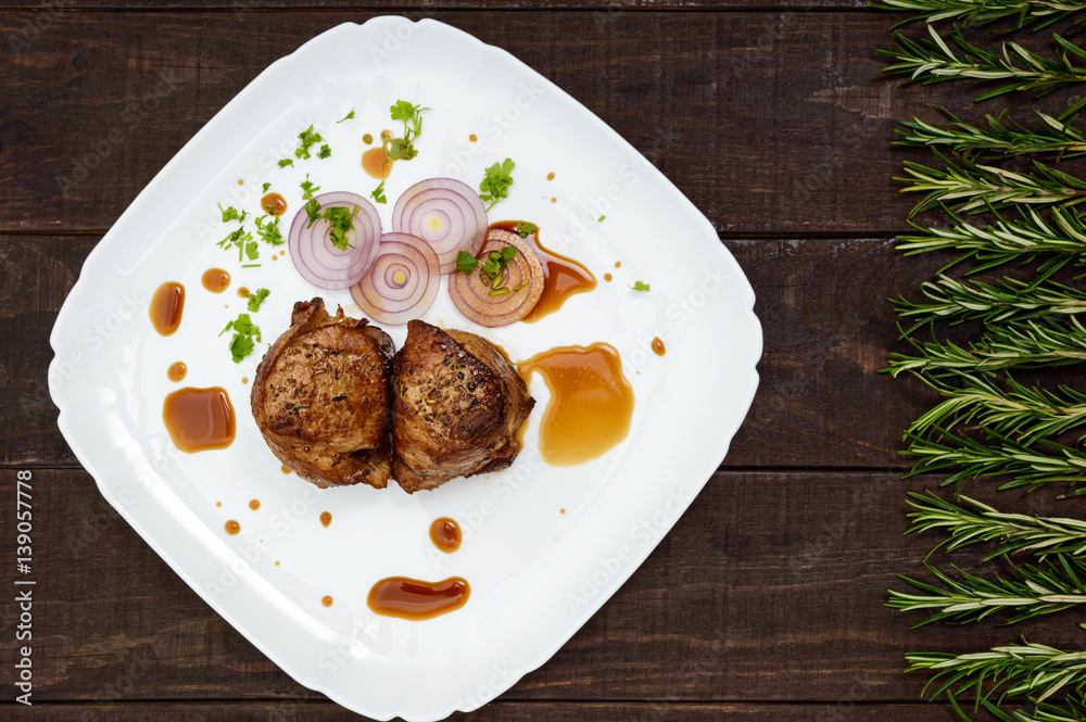 Juicy pork medallions wrapped in bacon on a plate on the dark wooden background. The top view. Juicy pork medallions wrapped in bacon on a plate on the dark wooden background. The top view.