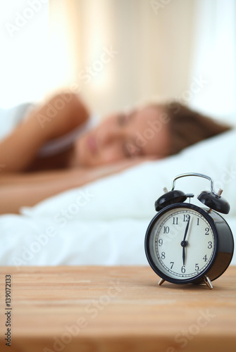 Young sleeping woman and alarm clock in bedroom at home