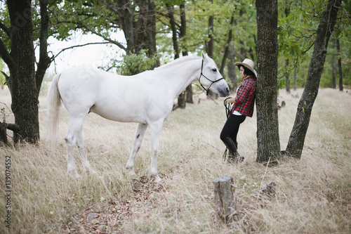 happy girl standing with her horse grazing nearby in the forest © anastasianess