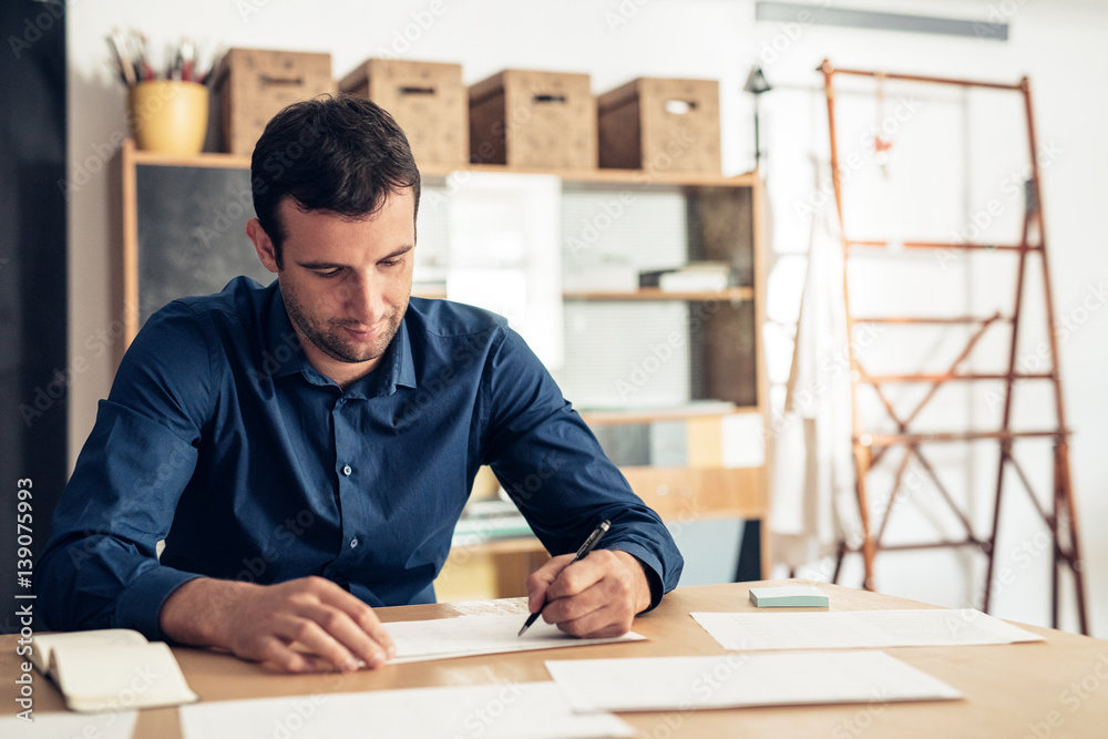 © mavoimages - Focused businessman writing on paperwork in a studio © mavoimages - Focused businessman writing on paperwork in a studio