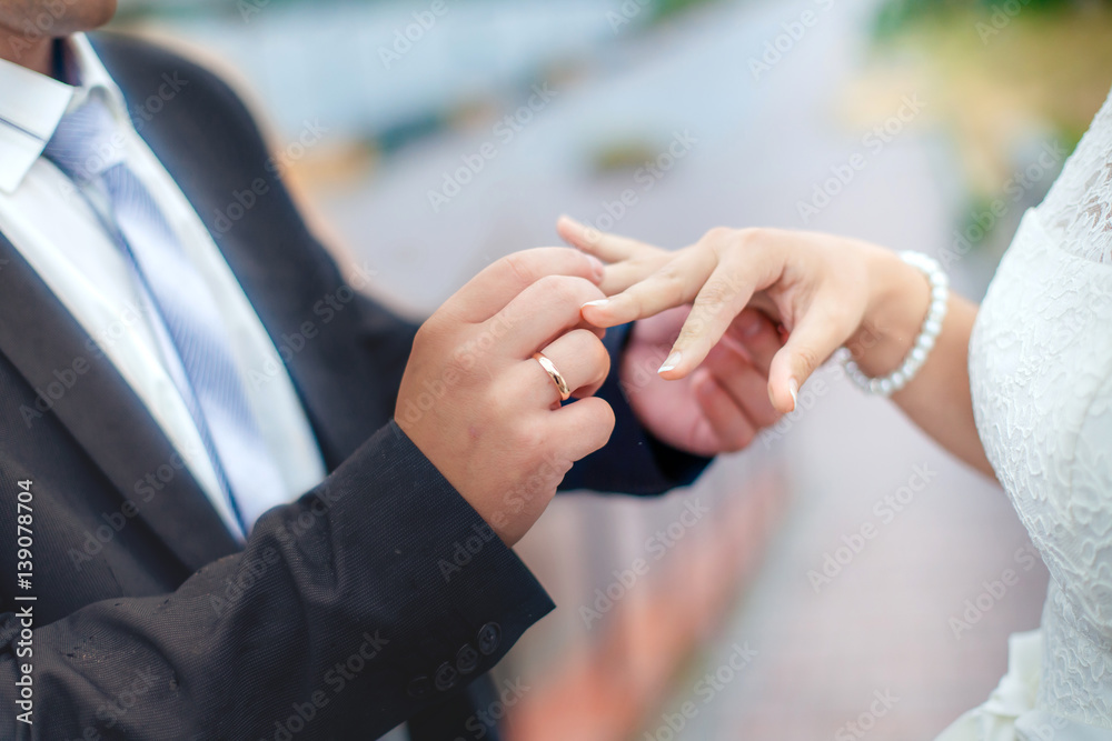 Fototapeta premium Groom wears bride a wedding ring on his finger. A couple betrothed in the street. Wedding ceremony - hands closeup.
