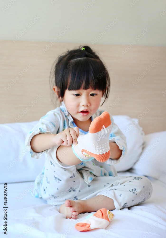Lovely little asian girl trying to put a socks on the bed. Lovely little asian girl trying to put a socks on the bed.