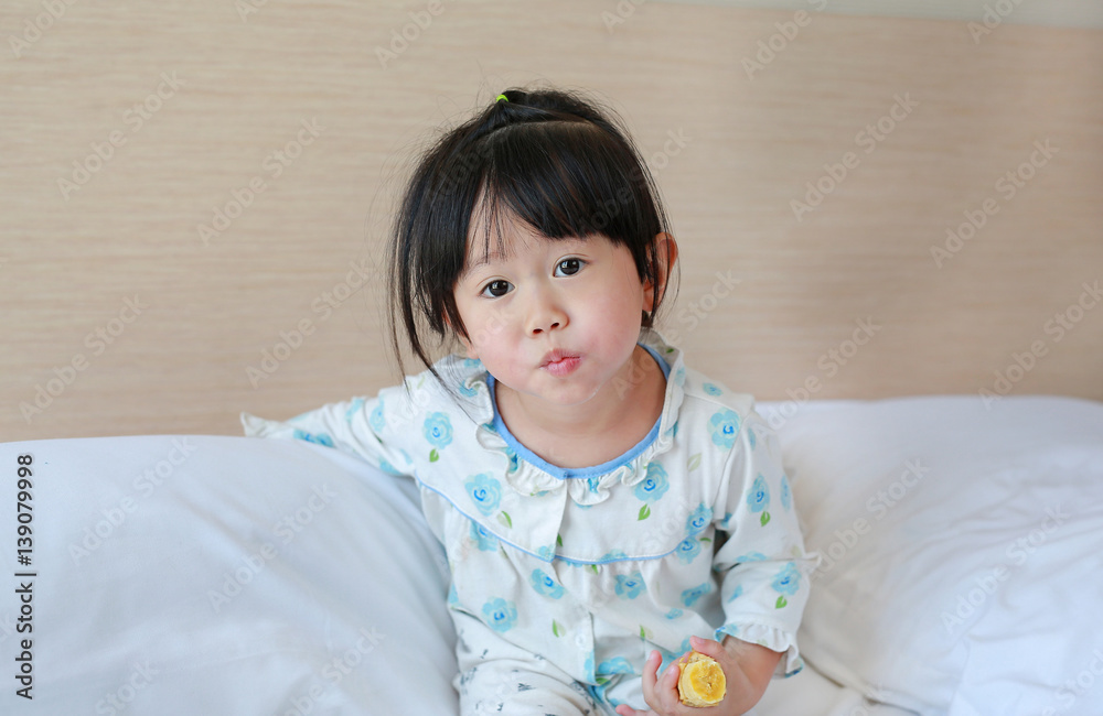 Cute Little girl in pajamas eating banana on the bed at the morning. Cute Little girl in pajamas eating banana on the bed at the morning.