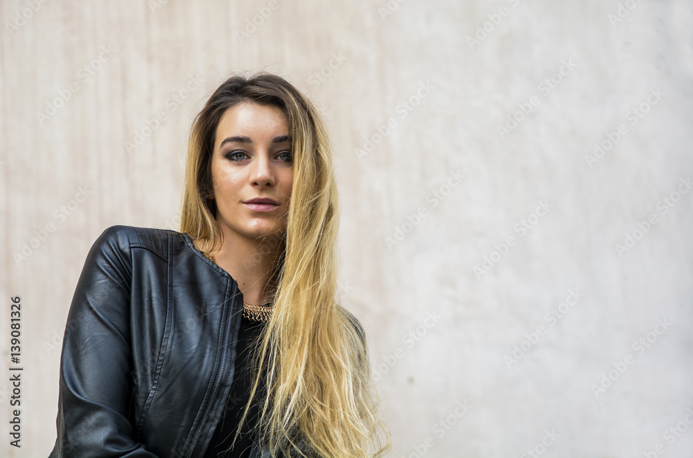 Portrait of attractive blonde young woman in black leather jacket, outdoor looking at camera