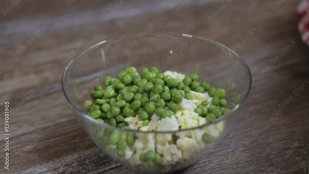 Cook adding green peas to the salad in a glass bowl close-up Cook adding green peas to the salad in a glass bowl close-up
