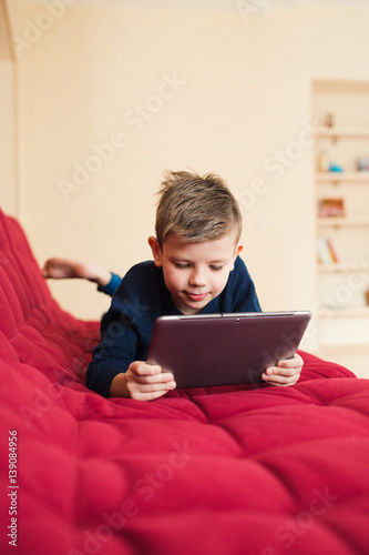 мальчик с планшетом лежит на диване у него дома © shapovalphoto