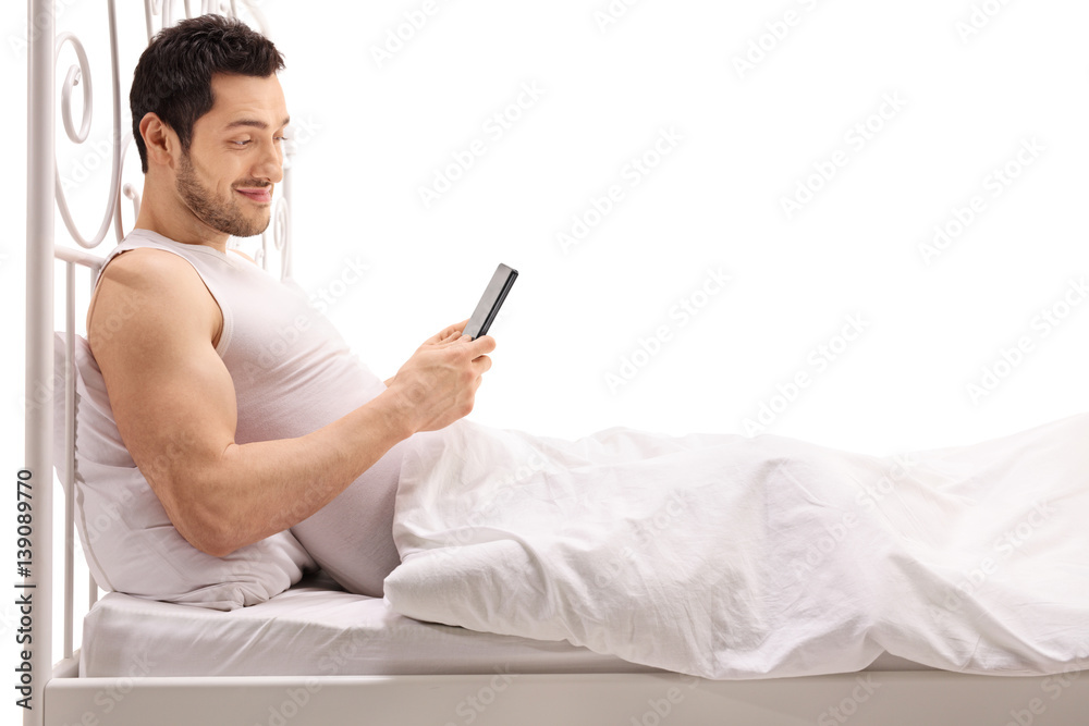 Young man using a phone while lying in bed Young man using a phone while lying in bed