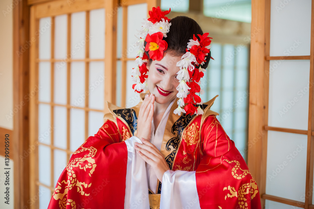 cosplay. beautiful, modest geisha in a red kimono posing in a Japanese  house with a fan Stock-Foto