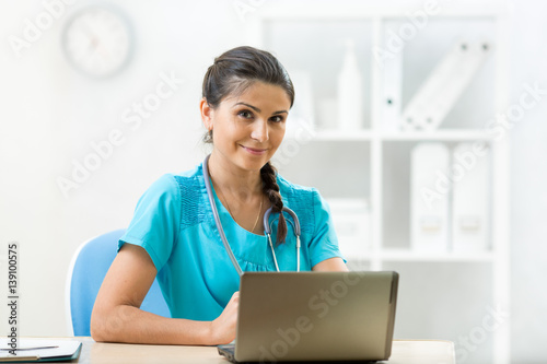 Smiling woman doctor sitting at desk in medical office