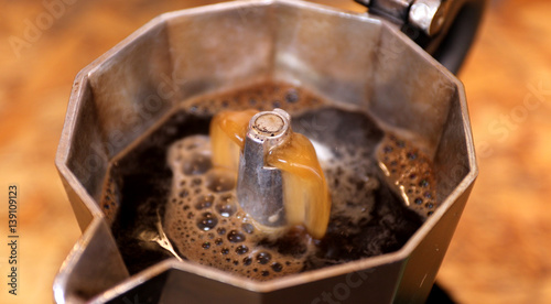 Closeup of frothy freshly percolated espresso coffee in moka espresso pot