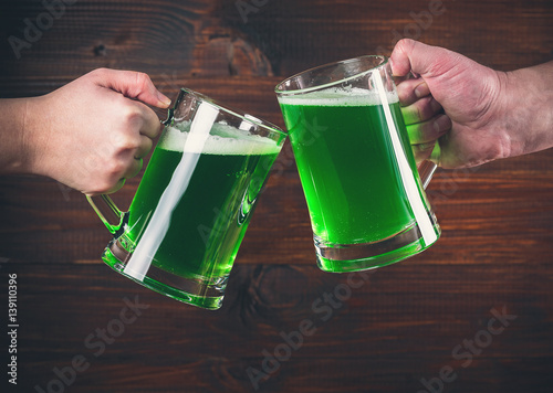 St Patrick's Day concept two mug on hands green beer against wooden background