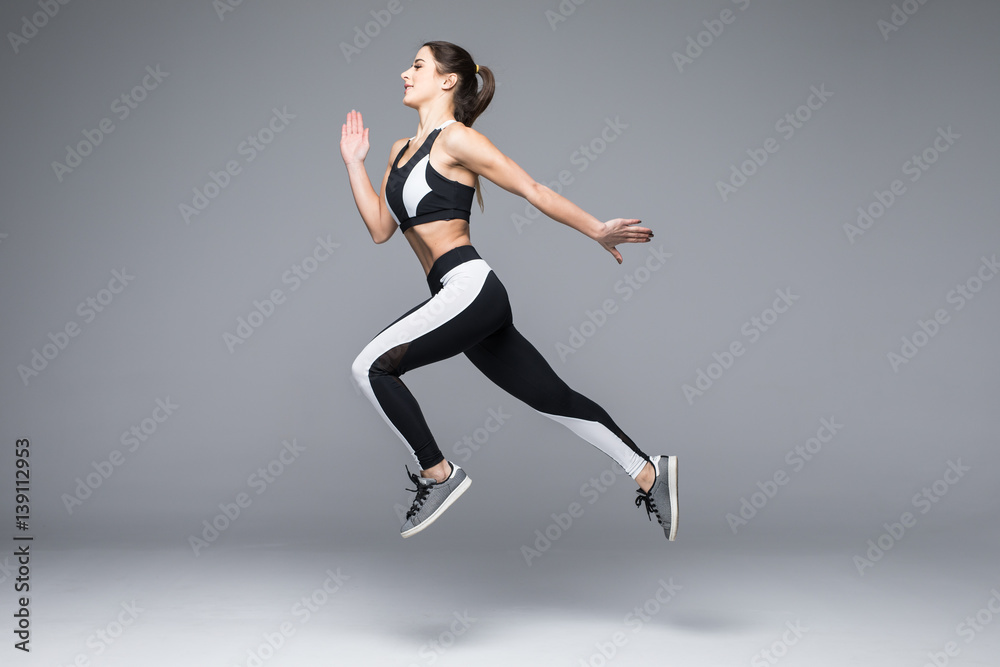 Side view of a sporty young woman jumping isolated on grey background
