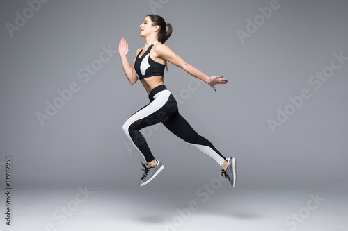 Side view of a sporty young woman jumping isolated on grey background